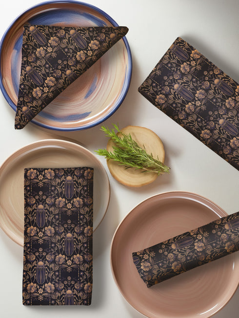 Set of four navy blue dining napkins featuring golden scarab beetles and botanical illustrations in a symmetrical pattern, sized 18x18 inches.